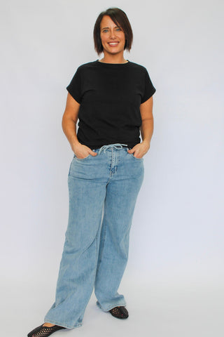 Woman wearing a black t-shirt and light blue jeans on a white background