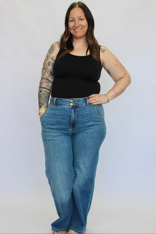 Woman wearing a black tank top and blue jeans against a white background