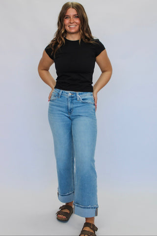 Woman wearing a black t-shirt and light blue jeans against a white background