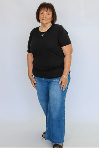 Woman wearing a black shirt and blue jeans against a white background