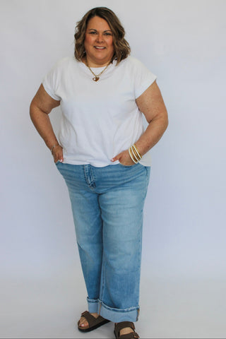 Woman wearing a white t-shirt and blue jeans against a plain background
