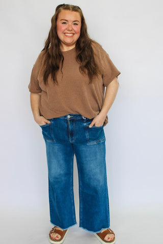 Person wearing a brown sweater and blue jeans against a white background