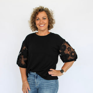 Woman wearing a black top with lace sleeves and blue jeans on a white background