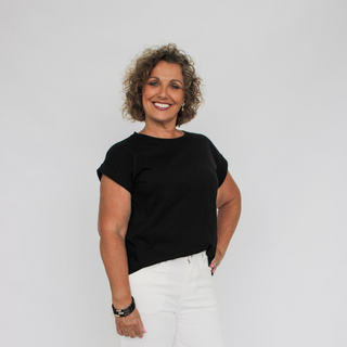 Woman wearing a black top and white pants against a plain background