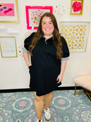 Woman wearing a black dress with white stripes in a room with decorative wall art.