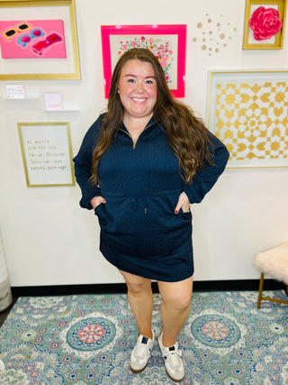 Woman wearing a navy blue dress standing in a room with decorative wall art.