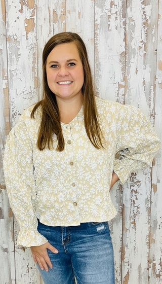 Woman in a floral blouse and blue jeans standing in a room with colorful artwork on the wall.