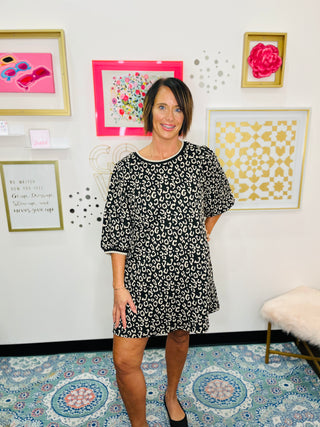 Woman in a cheetah patterned dress standing in a room with decorative wall art.