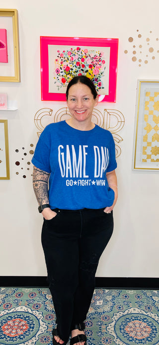 Woman wearing a blue t-shirt with 'GAME ON' text in a room with decorative wall art.