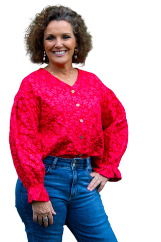 Woman wearing a bright red cardigan over a blue top with a green leafy background