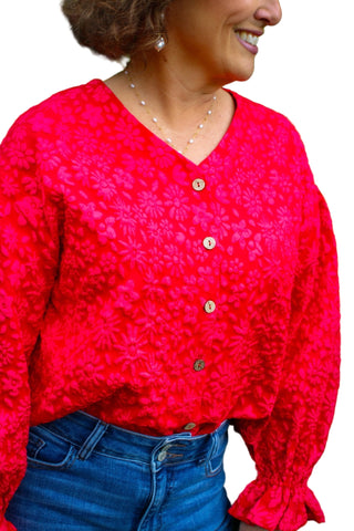 Person wearing a red textured blouse with a green leafy background