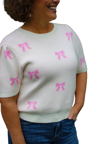 Person wearing a light-colored sweater with pink bow patterns against a green leafy background