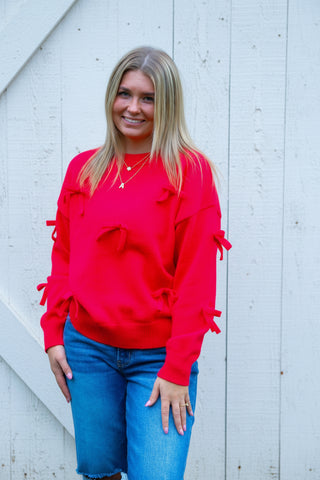 Woman wearing a red sweater and blue jeans standing in front of green bushes